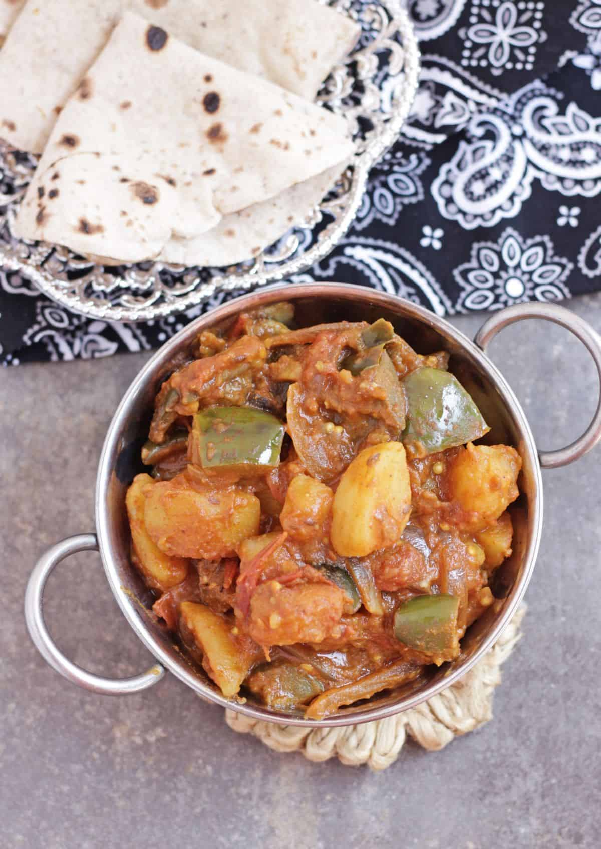 Aloo baingan curry in steel bowl with roti in the background.