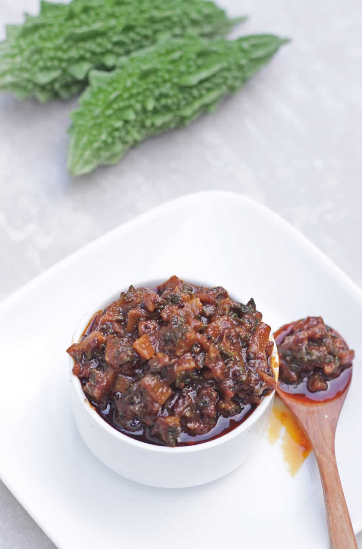 Pavakkai Urukkai in white bowl with pickle scooped out in wooden spoon