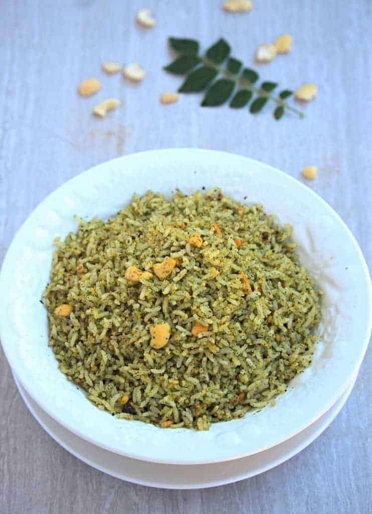 Karuveppilai Sadam in a white bowl with scattered cashews and fresh curry leaf in background